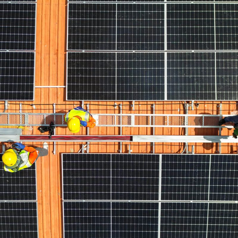 top aerial of engineer men inspects construction of solar cell panel or photovoltaic cell at roof top. Industrial Renewable energy of green power. factory at urban area. worker working on tower roof.